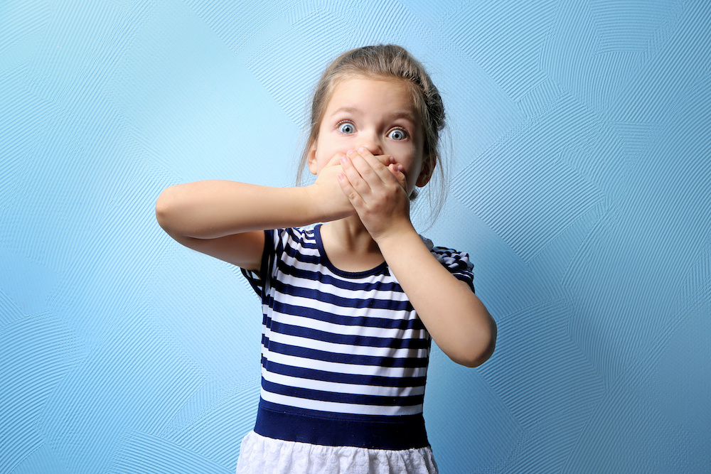 Cute little girl covering mouth with hands, on color background Learn how to avoid sugar bugs on your teeth when you have braces in Charleston SC