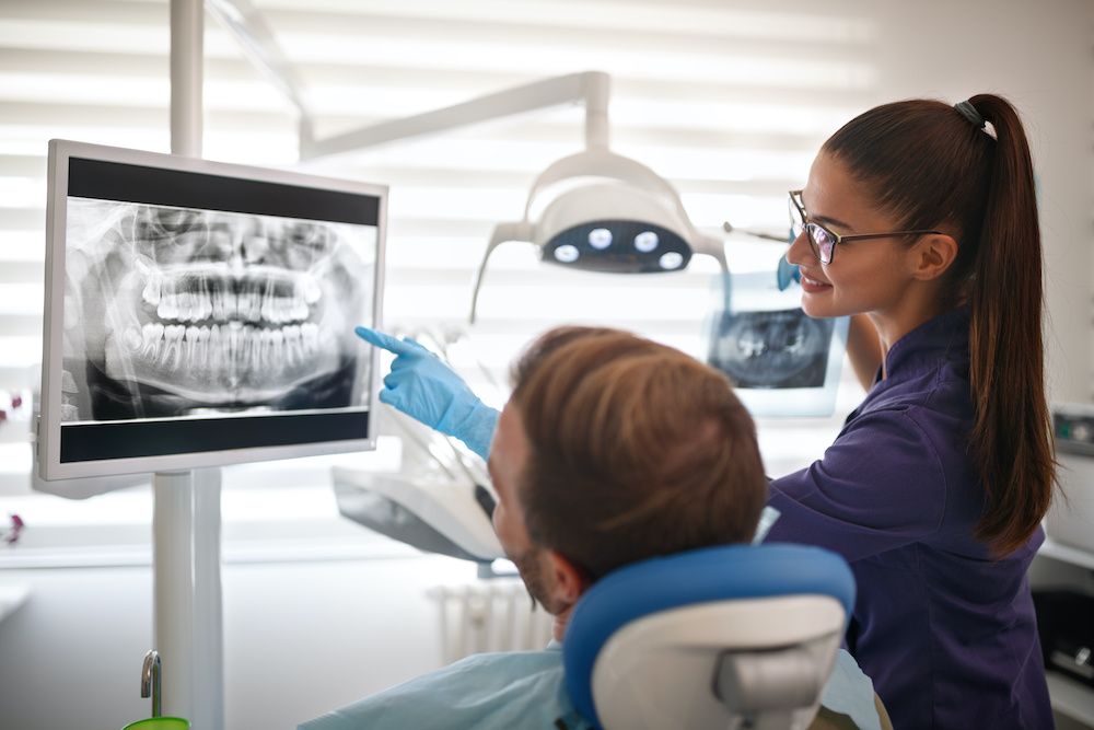 Dentist showing x-ray footage of teeth to patient Female dentist showing x-ray footage of teeth to male patient in clinic