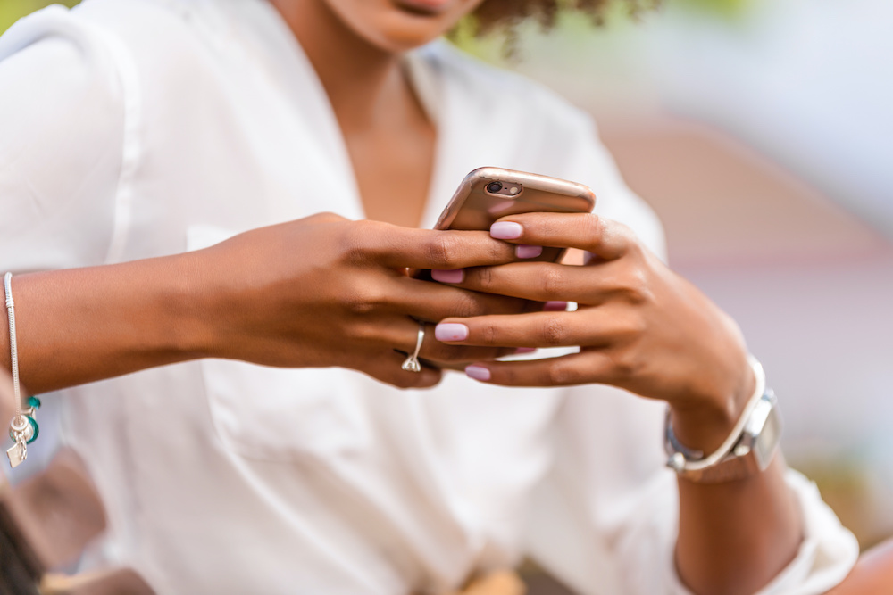 Outdoor portrait of a Young black African American young woman texting on mobile phone Do a virtual consult with an orthodontist in Mt Pleasant SC