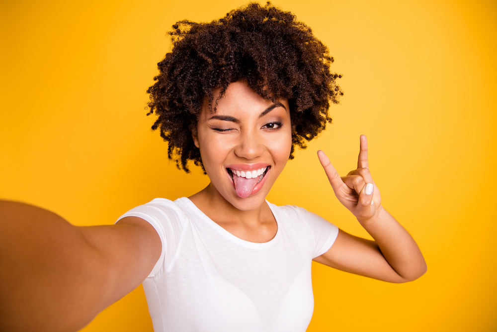 Close up photo beautiful amazing she her dark skin lady hand rock fan concert music lover tongue out mouth video translation wear casual white t-shirt isolated yellow bright vibrant vivid background Learn why and how you should brush your tongue with braces in Charleston SC